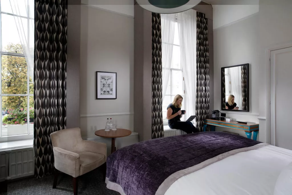 Queens Hotel Deluxe bedroom with person drinking coffee