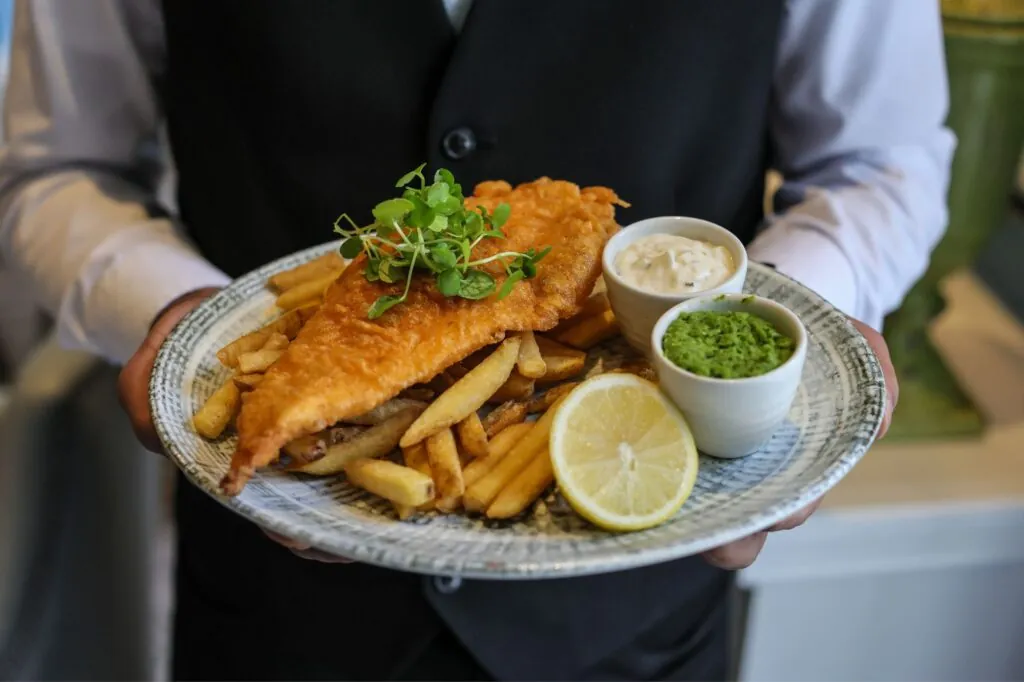 The Queens Hotel Cheltenham waiter holding crispy battered fillet of haddock